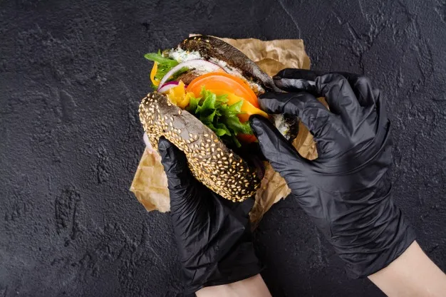 mains-femme-dans-gants-caoutchouc-noirs-tiennent-burger-pain-noir-juteux_107389-22.webp